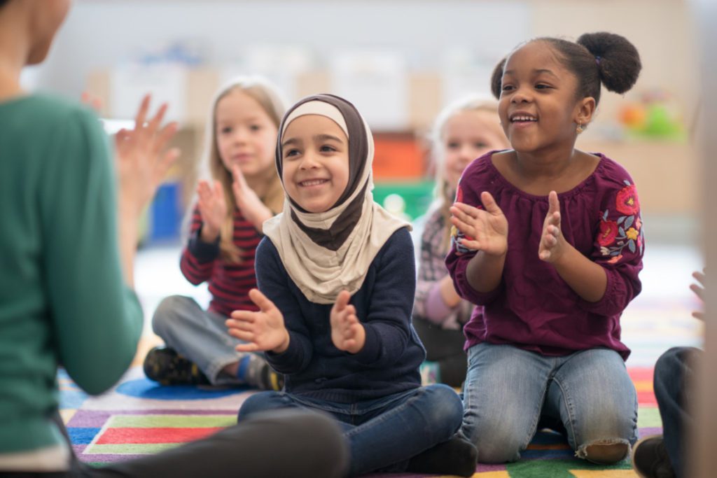 Young children in a classroom singing and clapping together.