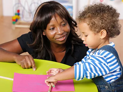 A teacher sits with a toddler at a small table