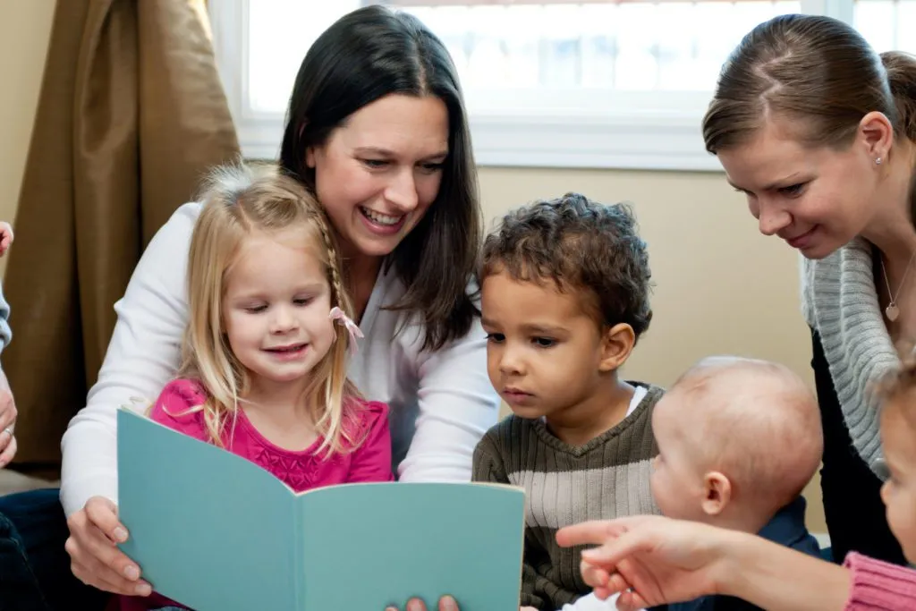 A teacher reads to a small group of children while a coach looks on