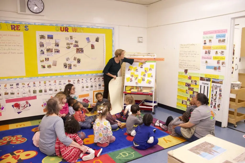 A teacher points to words as she reads off a chart during large group time