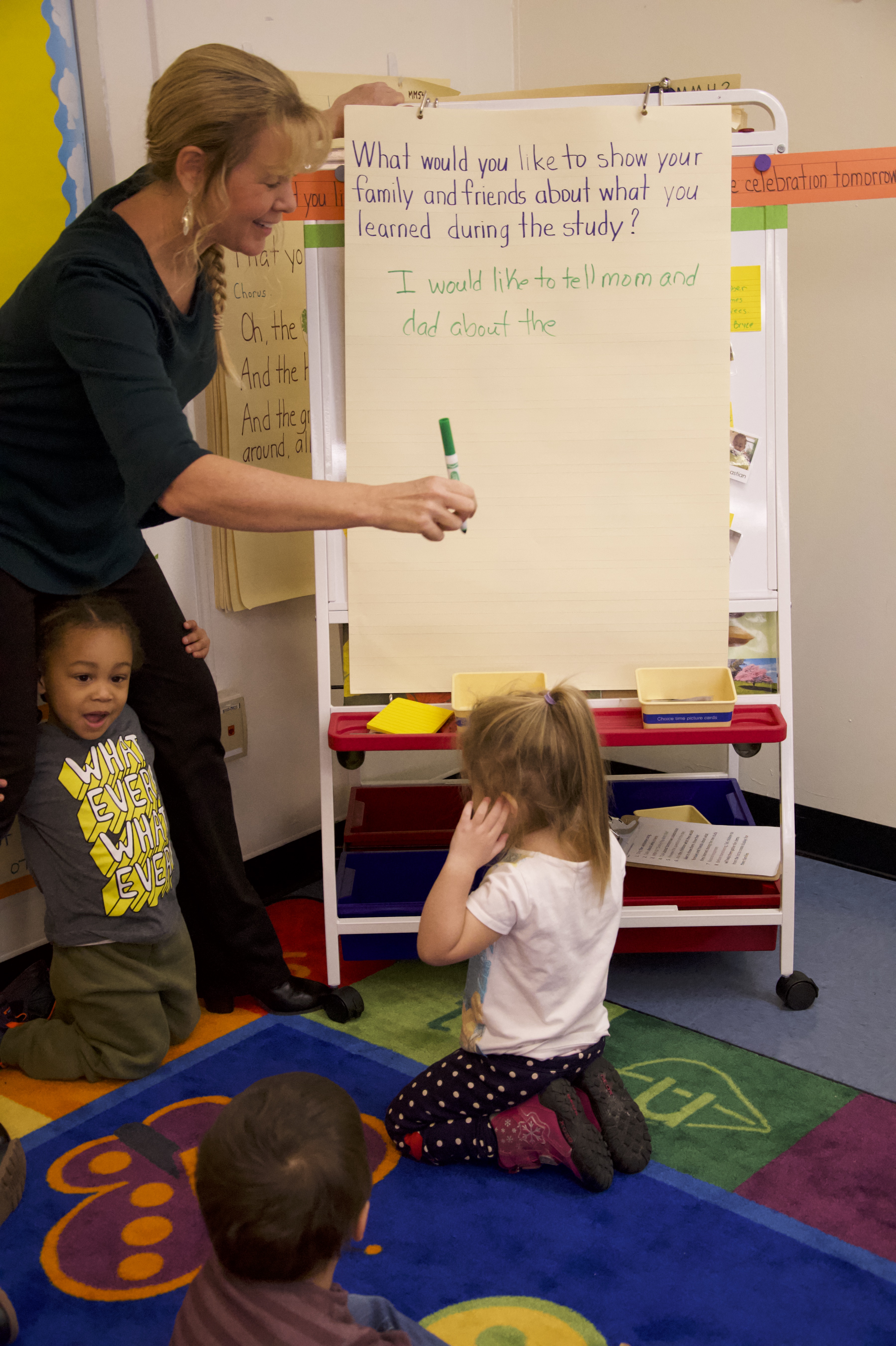 A teacher writes children's responses on the board during large group