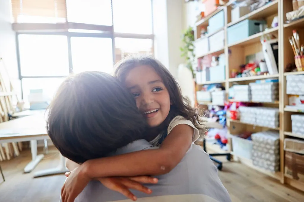 Young girl smiling and embracing her teacher in classroom