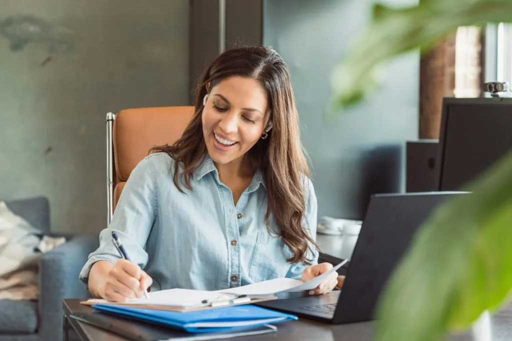 A teacher smiles as she takes notes during an online professional development session.
