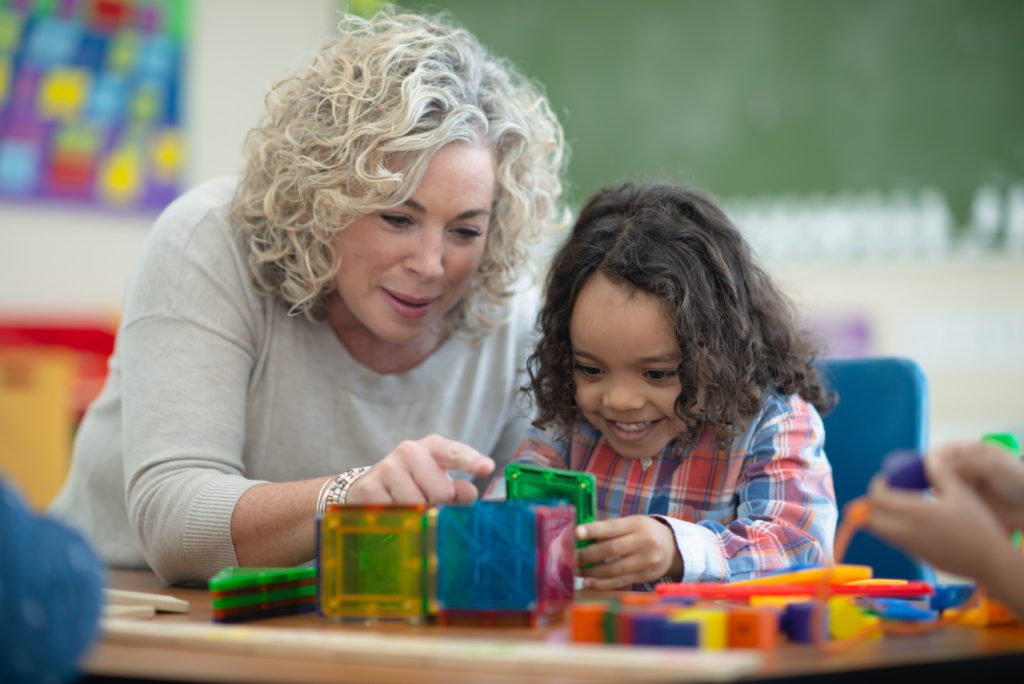Teacher and preschool child in the classroom building a cube and They are focused but also smiling and having fun.
