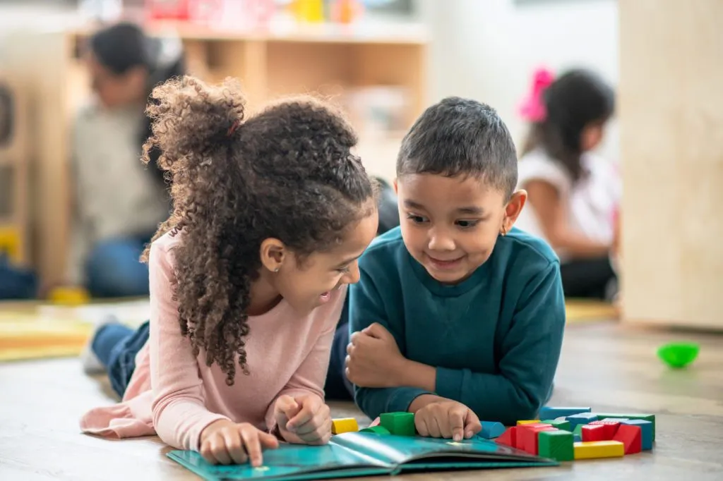 two children read a book together on the the daycare classroom floor.